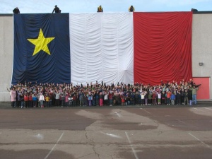Schoolchildren posing proudly in front of a giant Acadian flag